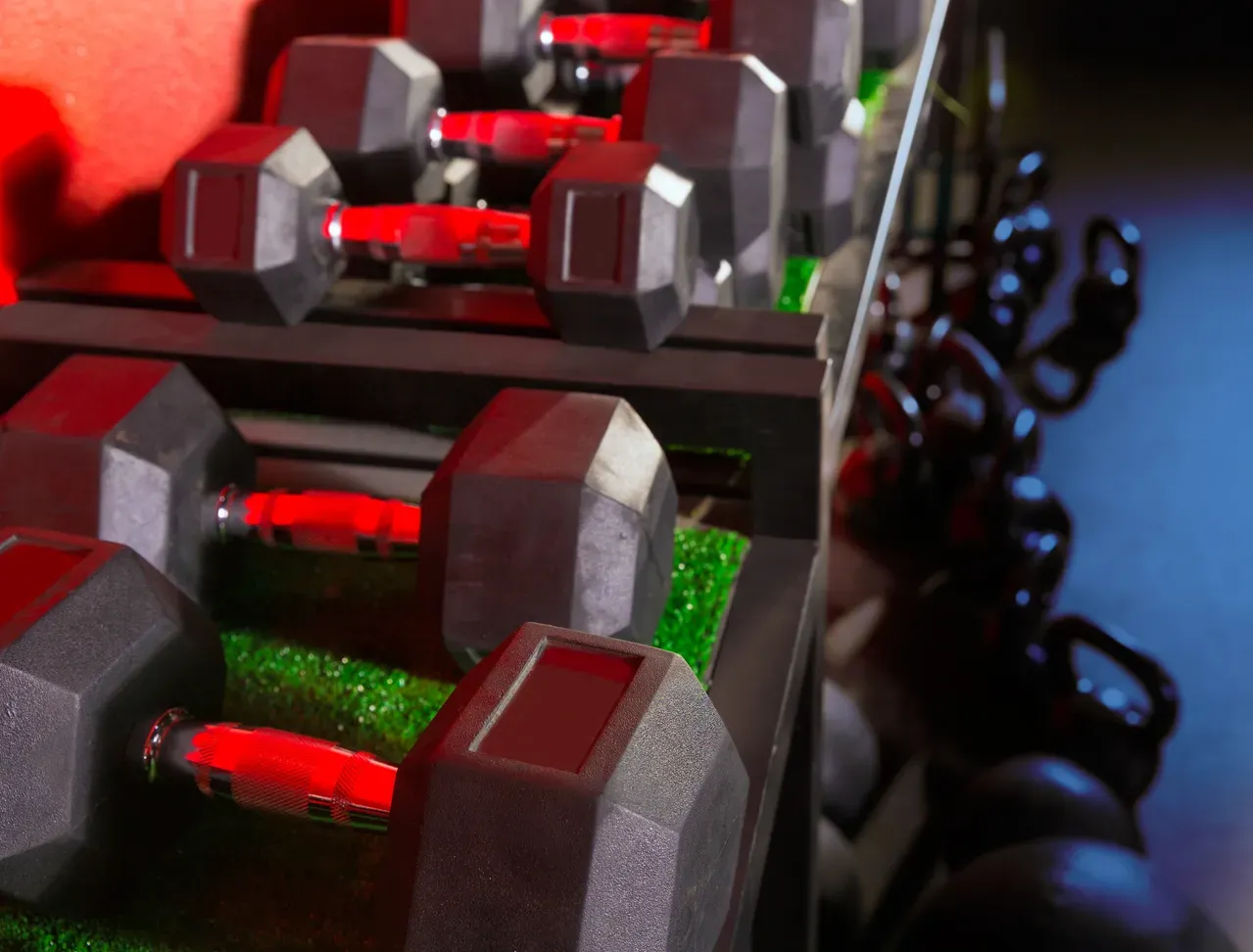 Close-up of hex dumbbells with red rubber grips on rack